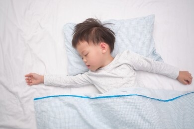 cute little asian 3 - 4 years old toddler boy kid in pajama taking a nap, sleeping on his back  on white bed sheet in bed, bedtime for kids concept with copy space