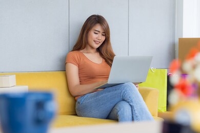 asian businesswoman is an e-commerce entrepreneur sitting on a chair, smile and are chatting with customers through laptop in her office. young woman's wearing casual cloth. business concept