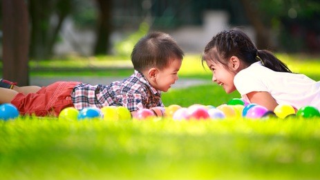two children, big syster and her young brother are laying on green grass and smile