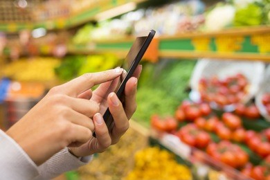 woman using mobile phone while shopping in supermarket, vegetable department store