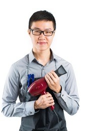 vertical portrait of a young professional stylist with a hairdryer in hands over a white background