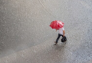 businessman in a very heavy rain walks down the street. is holding bag and red umbrella in hand. 