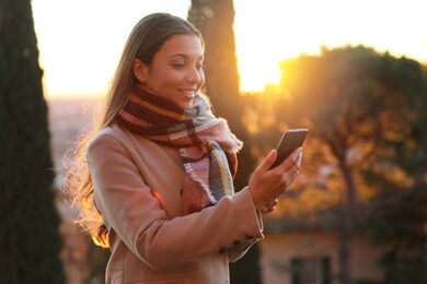 smiling beautiful woman using smart phone outdoor at sunset