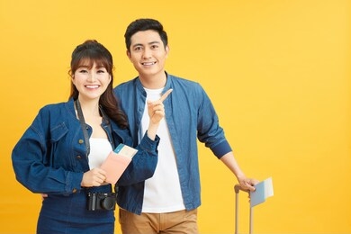 young travelling couple with suitcases pointing somewhere isolated on yellow