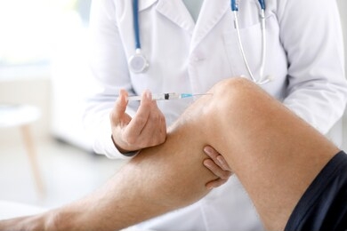 doctor giving sportsman with joint pain injection in clinic, closeup