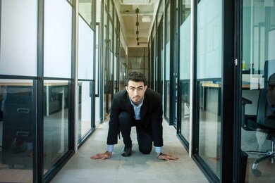 handsome asian businessman wearing a suit while crouching and preparing to run on the office hallway