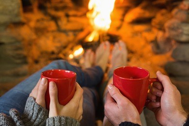 close-up of hands holding red coffee cups in front of lit fireplace
