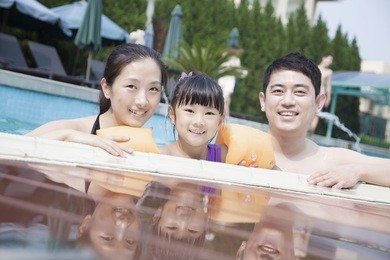 portrait of smiling family in pool by the edge looking at camera
