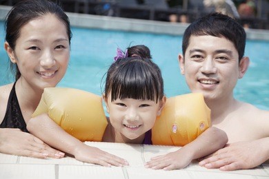 portrait of smiling family in pool by the edge looking at camera