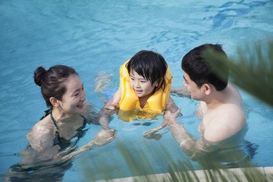 happy smiling family teaching son how to swim in  pool