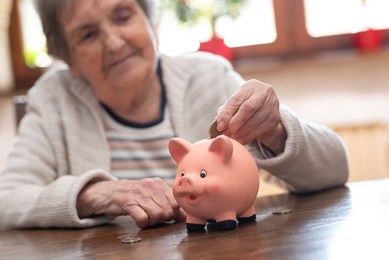 elderly woman putting a coin in a piggy bank