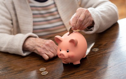 elderly woman putting a coin in a piggy bank