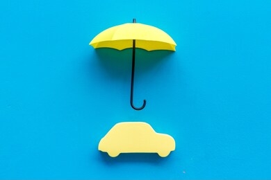 car insurance. automobile toy under umbrella on blue background top-down copy space