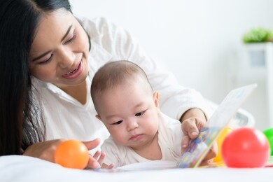 mother and baby relation of lovely family concept : portrait photo of asian mother reading and teaching her baby in bed.
