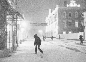 black-and-white picture of the city street during a snow-storm. some pedestrians hurry to take cover from a wind.