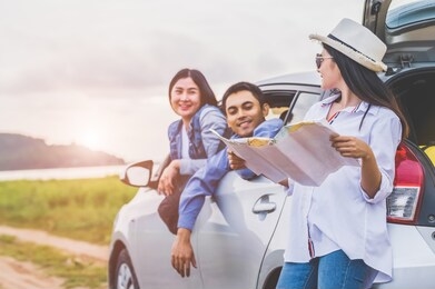 group of asian friends standing by car on coastal road at sunset. happy young friends having fun during road trip. people lifestyles and travel vacation concept. friendship journey and outdoor tour