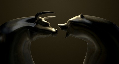 a closeup of two bronze castings depicting a stylized bull and a bear in contrasting light representing a financial market trends on an isolated dark background