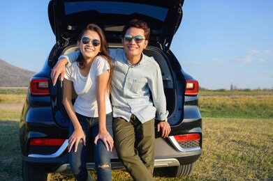 young couple happy asian out on a road trip. asian couple man  and woman sitting on back of car travel to mountain and lake in holiday with car road trip