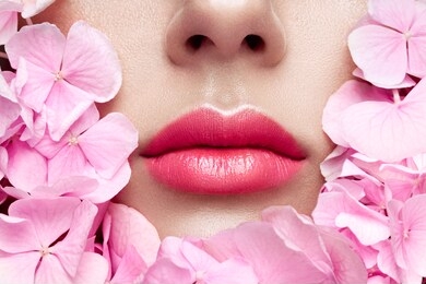 close up view of beautiful woman lips with pink lipstick in flowers. cosmetology, drugstore or fashion makeup concept. models face in decorated with flowers