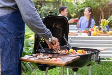 senior asian man wearing apron and having a barbecue party in the park.