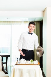 asian chinese room service waiter or steward serving guests food in a grand or luxury hotel room 