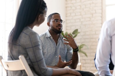 excited african american man in glasses sit in circle at team therapy session talking sharing thoughts or ideas, motivated biracial male counseling diverse people at group psychotherapy treatment