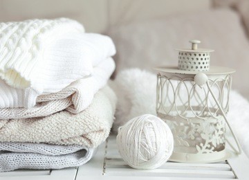 stack of cozy knitted sweaters and lantern on a table