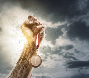 success concept, male hand rise up a gold medal against the dramatic sky with copy space
