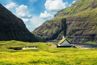 summer view of traditional turf-top church saksunar kirkja in saksun village. beauty landscape with pollurin laguna and high mountains. streymoy island, faroe islands, denmark.