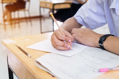 asian students holding pencil in hand doing multiple-choice quizzes or testing exams answer sheets exercises on old wood table in secondary school, college university classroom in education concept.