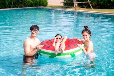 asian mother and father play with her daughter in a swimming pool in a tropical resort, this image can use for family, girl, summer and relax concept.