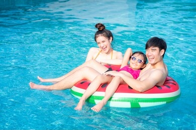 asian mother and father play with her daughter in a swimming pool in a tropical resort, this image can use for family, girl, summer and relax concept.