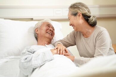 loving and caring senior asian woman visiting and talking to hospitalized husband at bedside