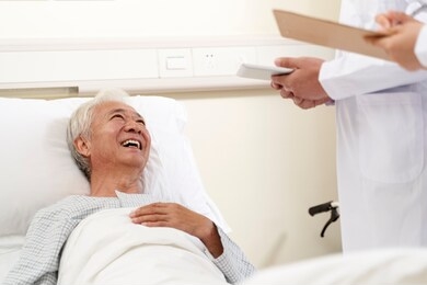happy asian old man lying in hospital bed talking to doctors