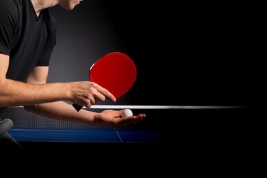 portrait of young man playing tennis on black background. table tenns player serving 