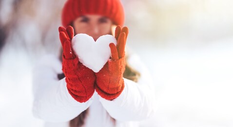 woman in red gloves and hat holding heart shape from snow, valentines day, sun set. love concept.