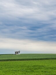 lonely small abandoned house on green field with an angry sky
