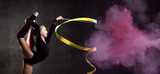 portrait of beautiful young brunette woman gymnast training calisthenics exercise with yellow ribbon on dark pink smoke studio background. art gymnastics concept
