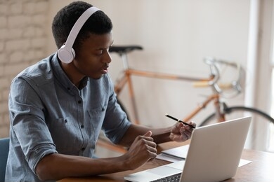african american businessman wearing headset using laptop, working online, manager consulting client customer, making video call, trainee intern watching webinar, writing notes, listening to lecture