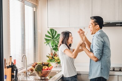 romantic asian couple in love is singing and dancing while cooking together in kitchen