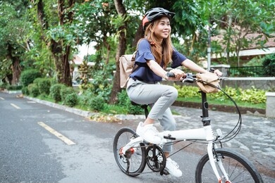 asian young woman goes wearing a helmet and a bag riding her folding bicycle on the road