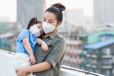 asian mother and little young daughter wearing mask for prevent dusk pm 2.5 bad air pollution on deck in bangkok city thailand 2020. 
