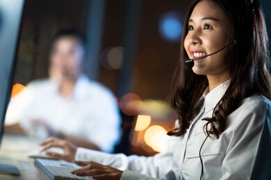 asian woman work as customer support service or call center phone operator, using desktop computer and microphone headset, late night shift. overtime office life, telemarketing or sales job concept