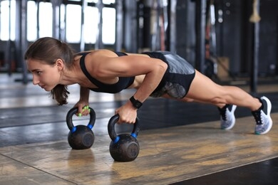 portrait of a muscular woman on a plank position with kettlebell at gym.