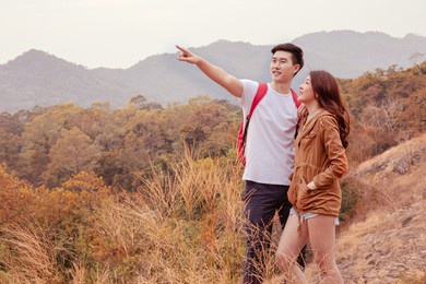 selective focus, asian affectionate couple hold together in forest field pointing hands destination or showing beautiful nature/ man, beautiful woman happy spent time holiday, couple traveling concept