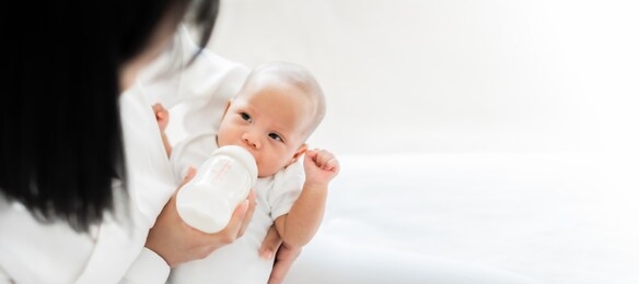 mother feeding asian baby with bottle of milk, banner copy space