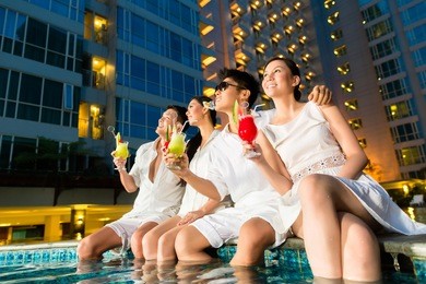 two young and handsome asian chinese couples or friends drinking cocktails in a luxurious and fancy hotel pool bar 