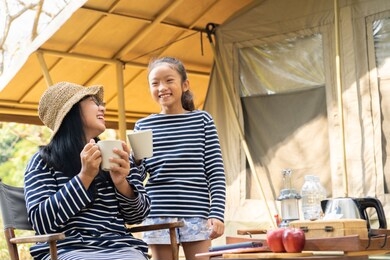 asian mom and daughter enjoy drink at campsite, concept  happy family time camping outdoors