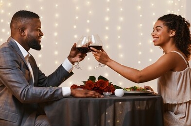 handsome black man and pretty afro woman drinking wine at restaurant, toasting and celebrating valentine's day, copy space