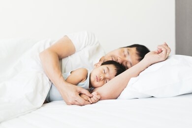 cute asian little baby boy is peaceful sleep on his father's arm in the white bedroom, concept of love and relation of daddy to the child in family lifestyle.